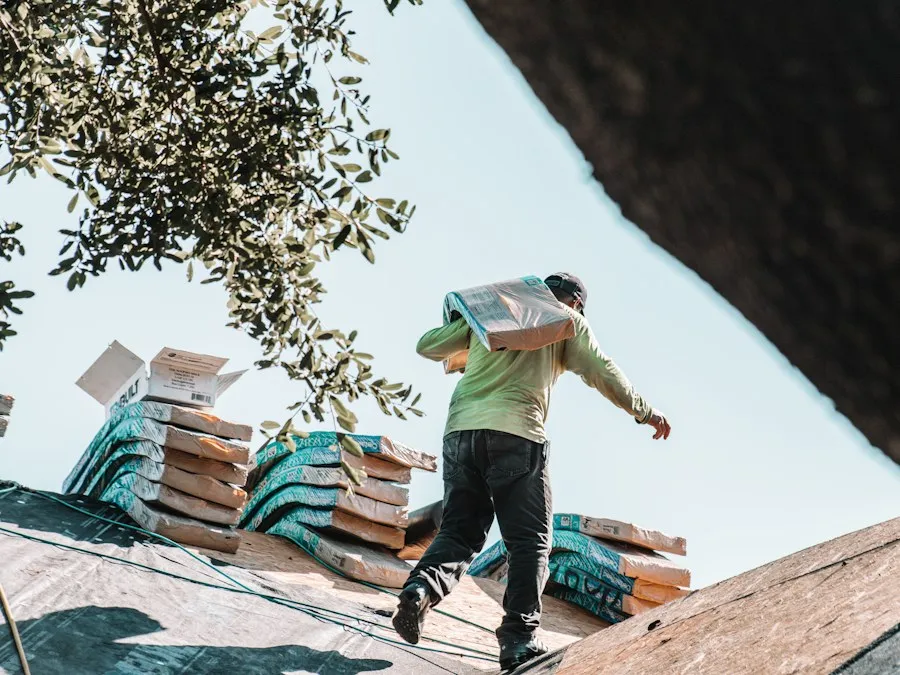 A roofer carrying a bundle of shingles across a roof.